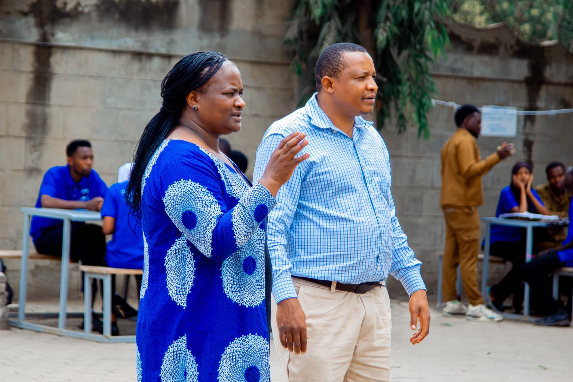Two Datasky College staff members in conversation on the college grounds with students behind them